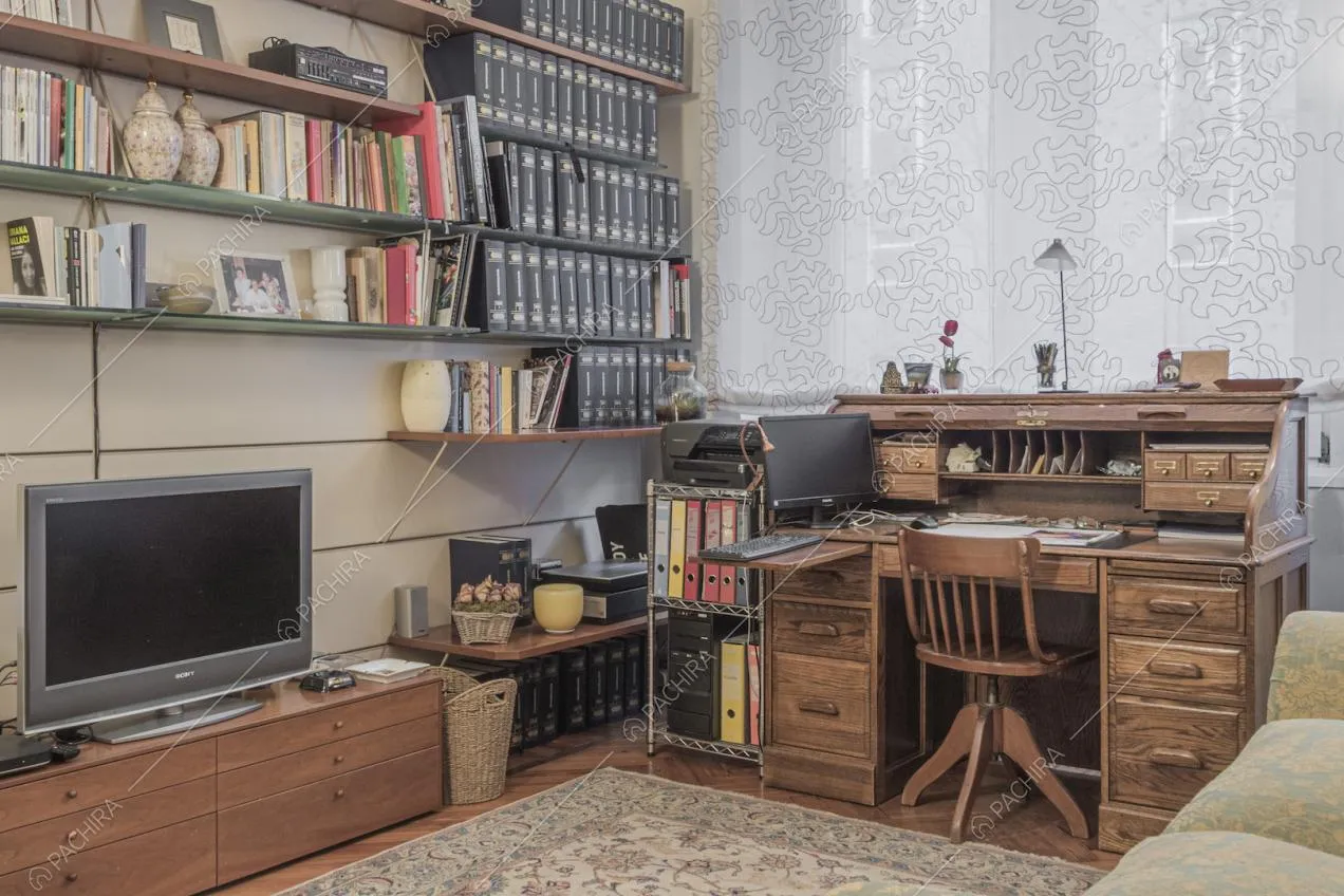 Studio con scrivania, mensole piene di libri e televisore