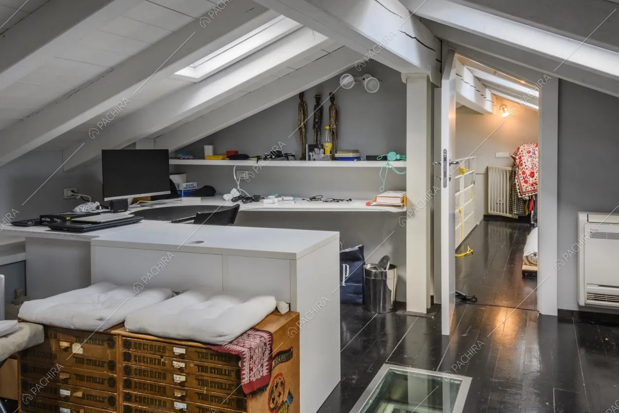 Angolo studio nella mansarda con travi a vista dipinte di bianco e pareti grigie