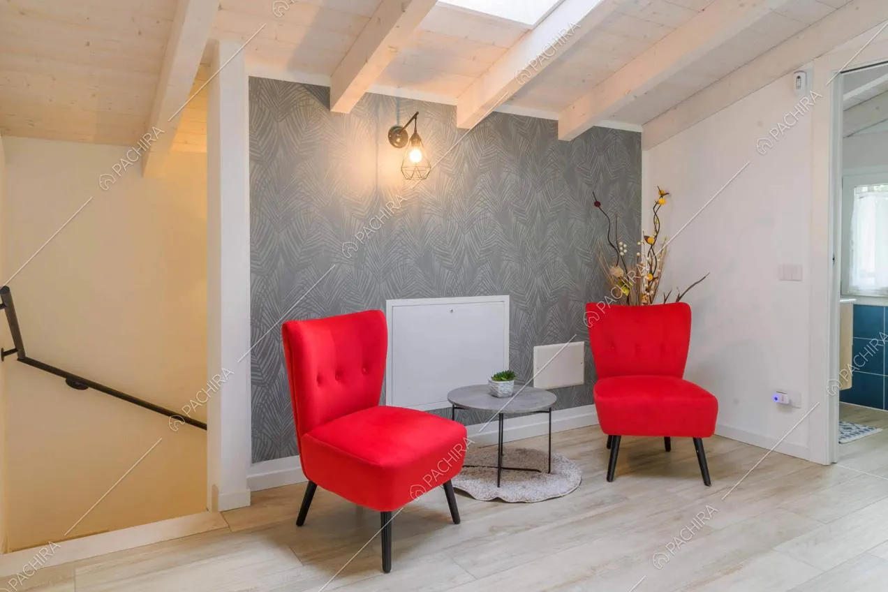 Atrio con carta da parati grigia, poltron e rosse, lucernario e soffitto bianco in travi in legno a vista