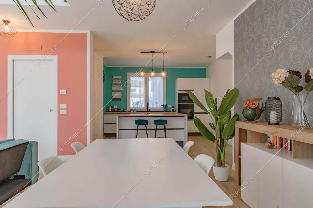 Tavolo da pranzo bianco nella sala e vista sulla cucina a isola con parete verdeacqua