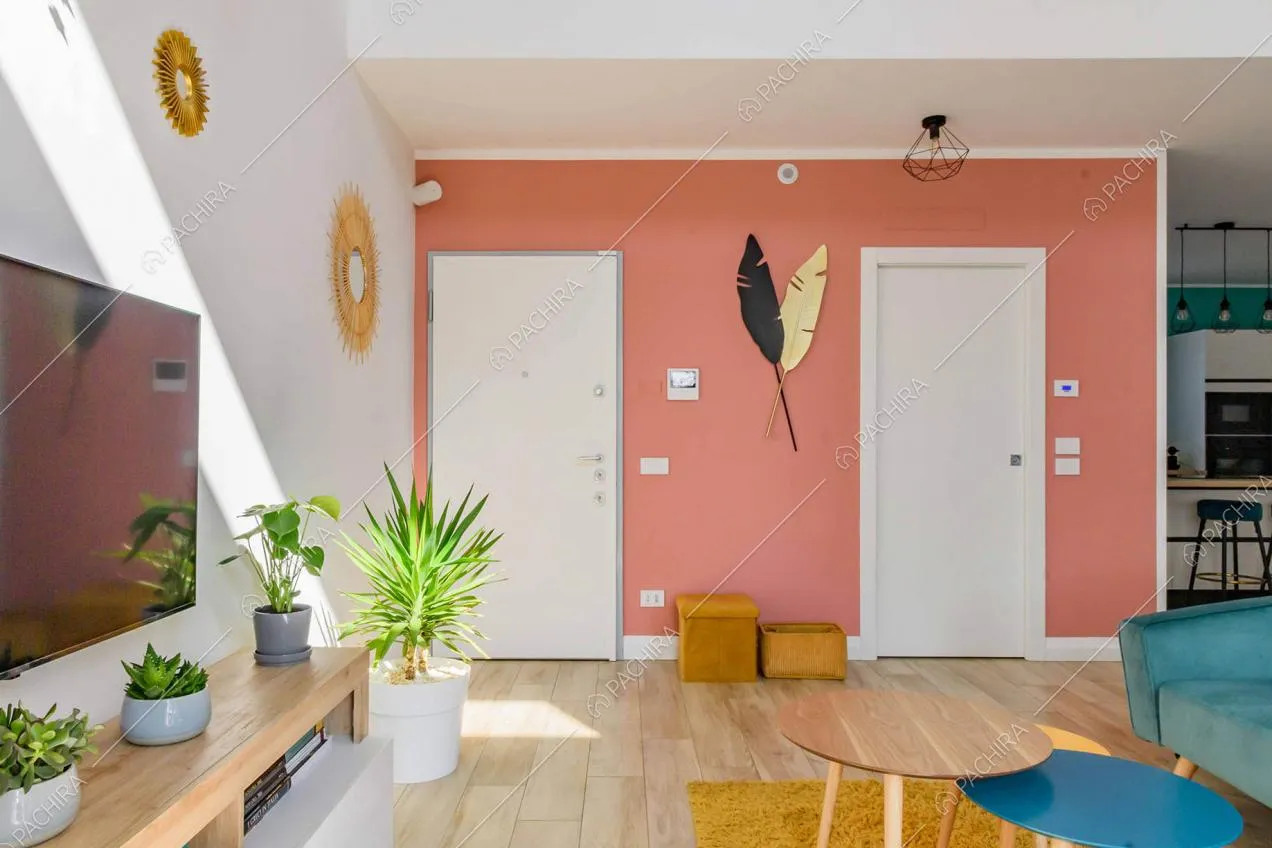 Salotto con tavolini in legno e vista sulla porta d'ingresso con parete rosa
