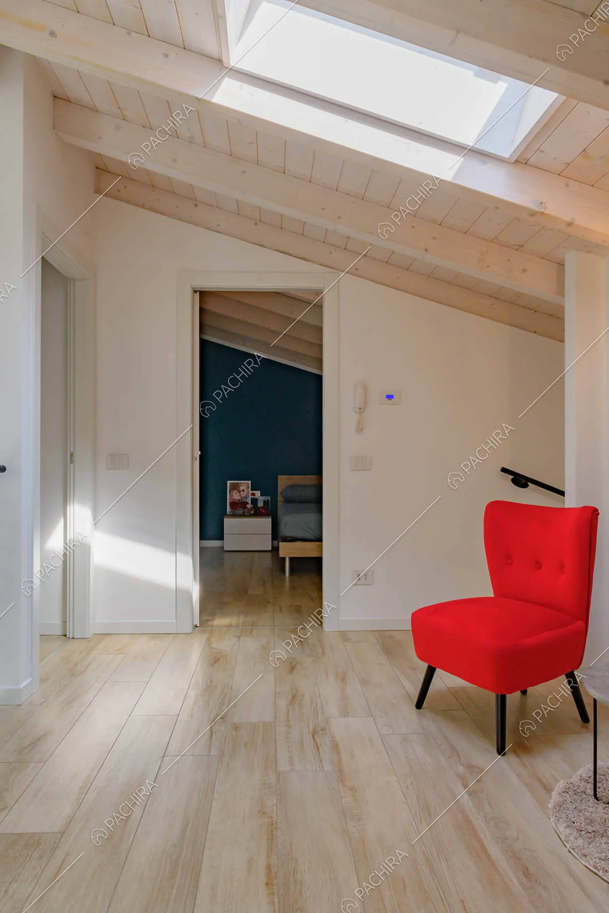 Poltrona rossa nell'atrio con lucernario, pavimento in parquet e vista sulla camera da letto matrimoniale