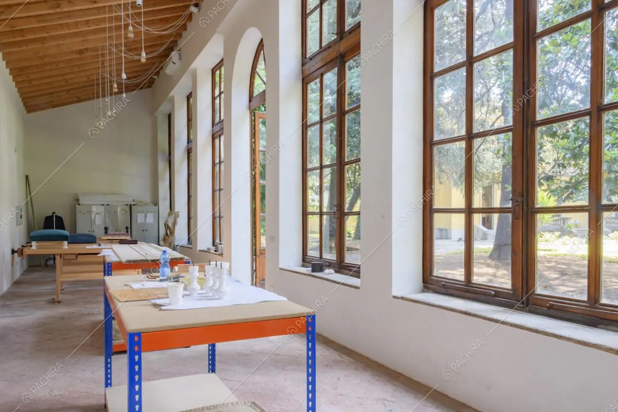 Interno della limonaia dalle pareti bianche, soffitto con travi in legno a vista e ampie e numerose finestre
