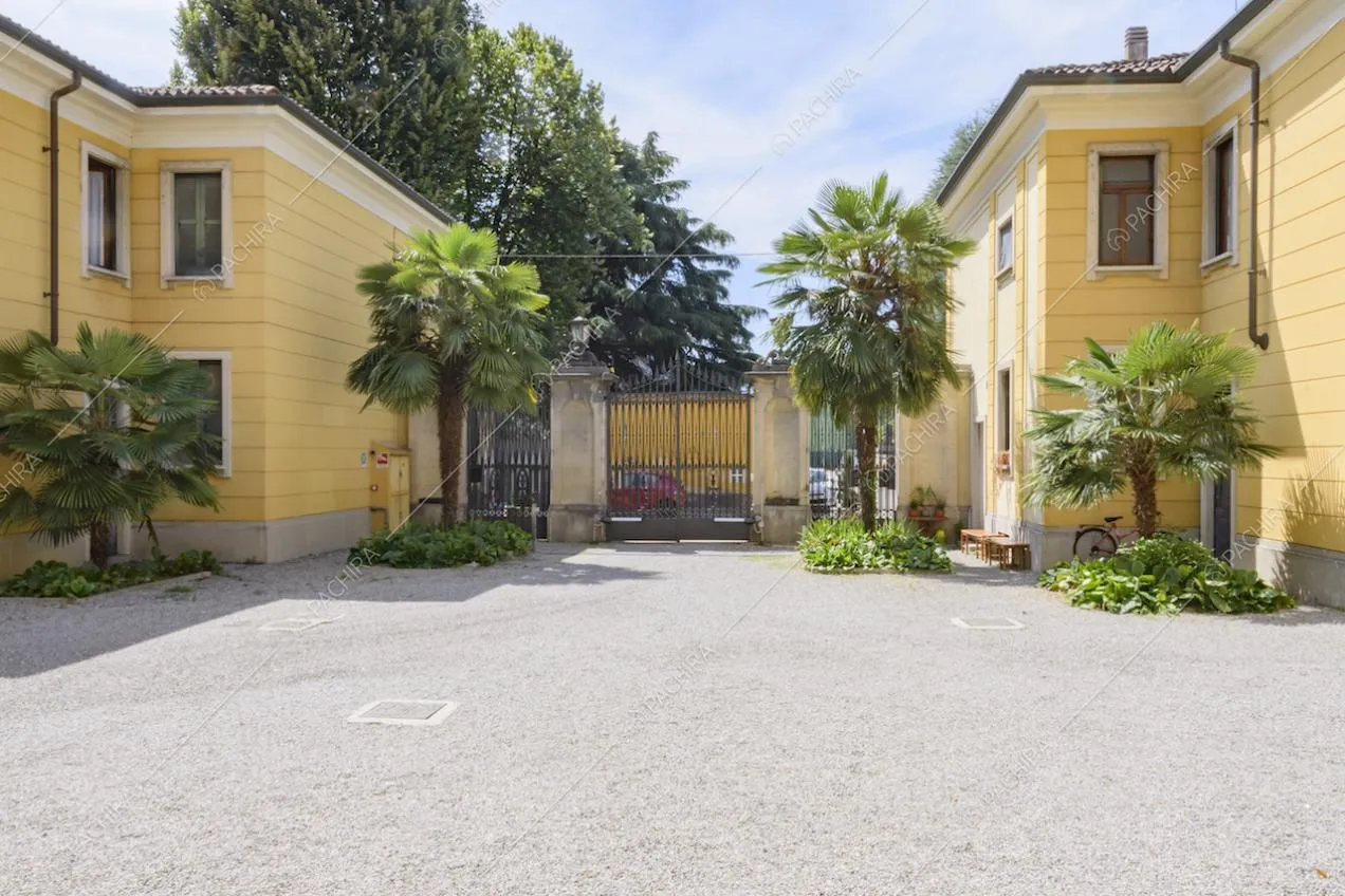 Ingresso dal cancello della villa con palme e vista sulle facciate gialle