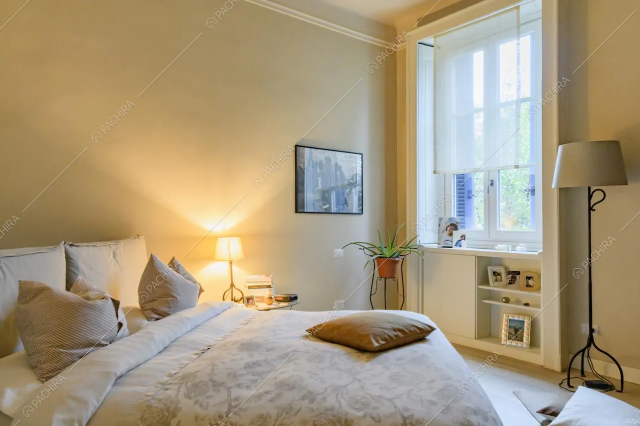 Luminosa camera da letto matrimoniale dalle pareti beige con boiserie e pavimento in parquet