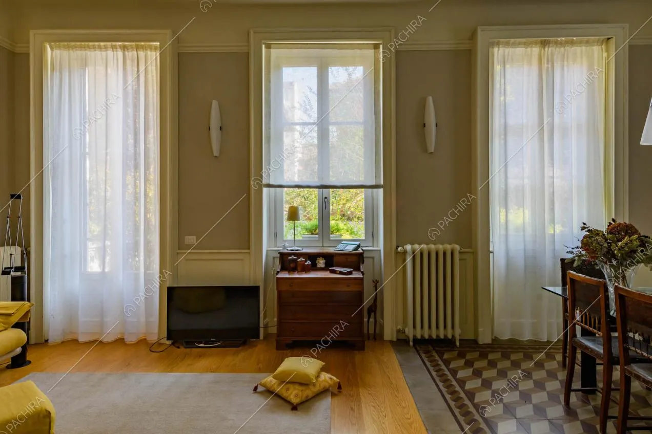 Sala con divano in parquet e in marmo, grandi vetrate e pareti grigie con boiserie