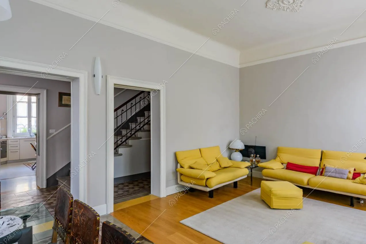 Salotto con boiserie sul soffitto, pareti grigie, divani gialli e vista sulle scale e sulla cuicna