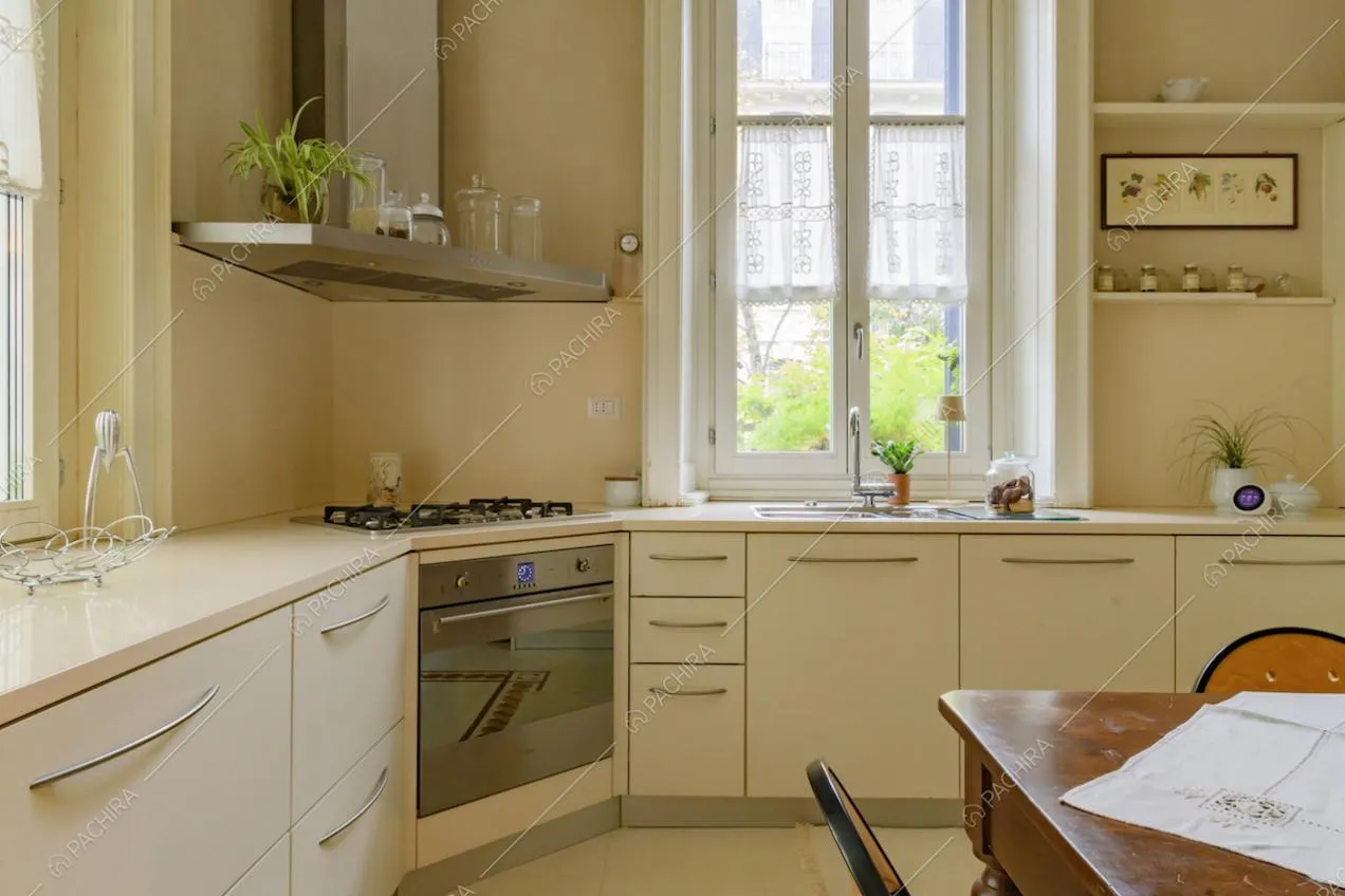 Luminosa cucina bianca a parete con fornelli a gas e tavolo da pranzo in legno
