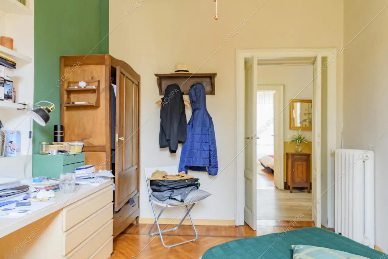 Dal letto nella camera con parete verde e pavimento in parquet a spina di pesce vista sul corridoio
