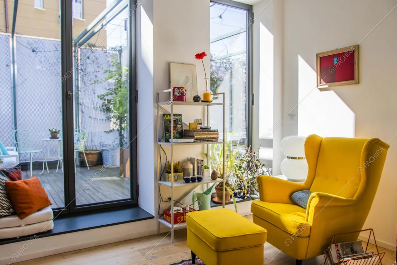 Studio con porta-finestra per accedere alla terrazza, pareti bianche, pavimento in parquet e poltrona gialla con poggiapiedi