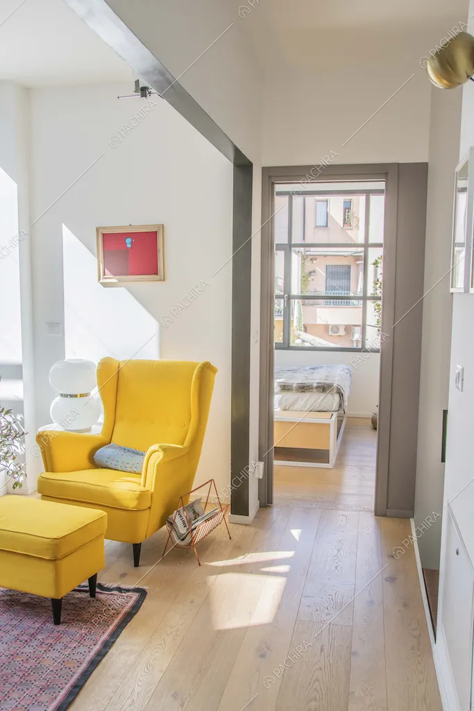 Studio con pavimento in parquet, poltrona gialla di design e vista su camera da letto