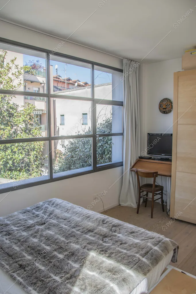 Camera da letto matrimoniale con finestra in stile industriale, scrivania e pavimento in parquet