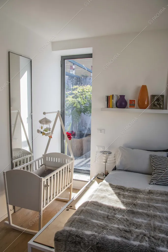 Luminosa camera da letto matrimoniale con culla, pavimento in parquet e pareti bianche