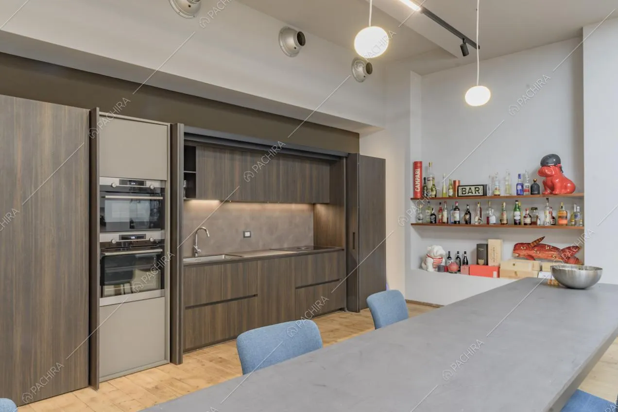 Dal tavolo da pranzo vista sulla cucina a muro in legno con fornelli a induzione