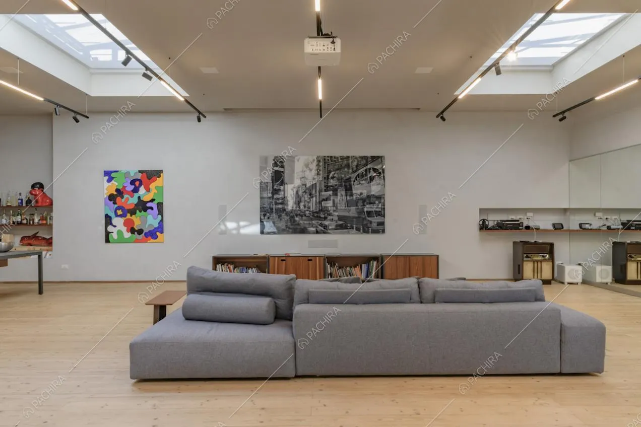 Divano grigio nell'ampia sala illuminata da lucernari e con pavimento in parquet