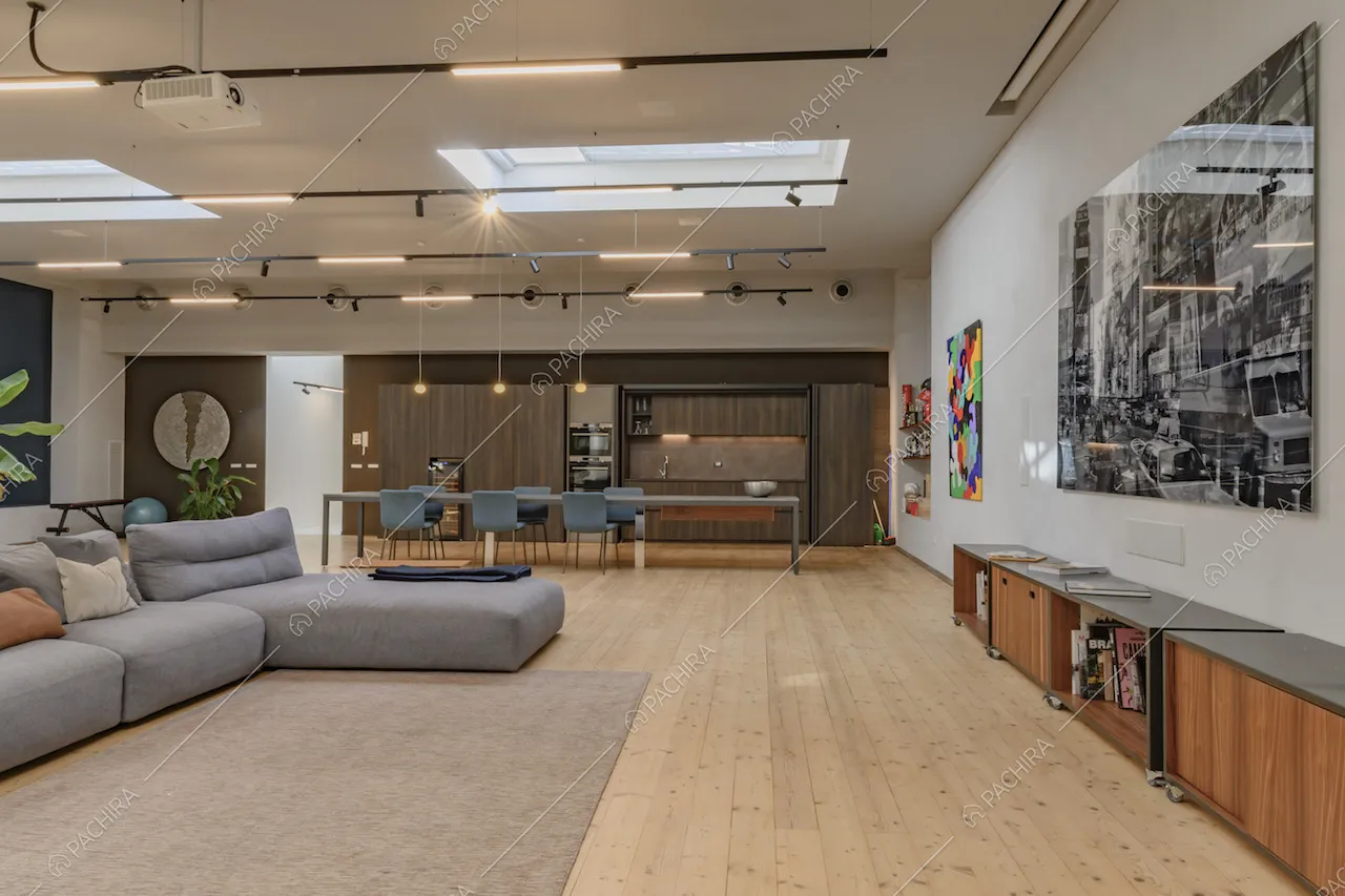 Sala con divano angolare grigio e pavimento in parquet illuminata da lucernari