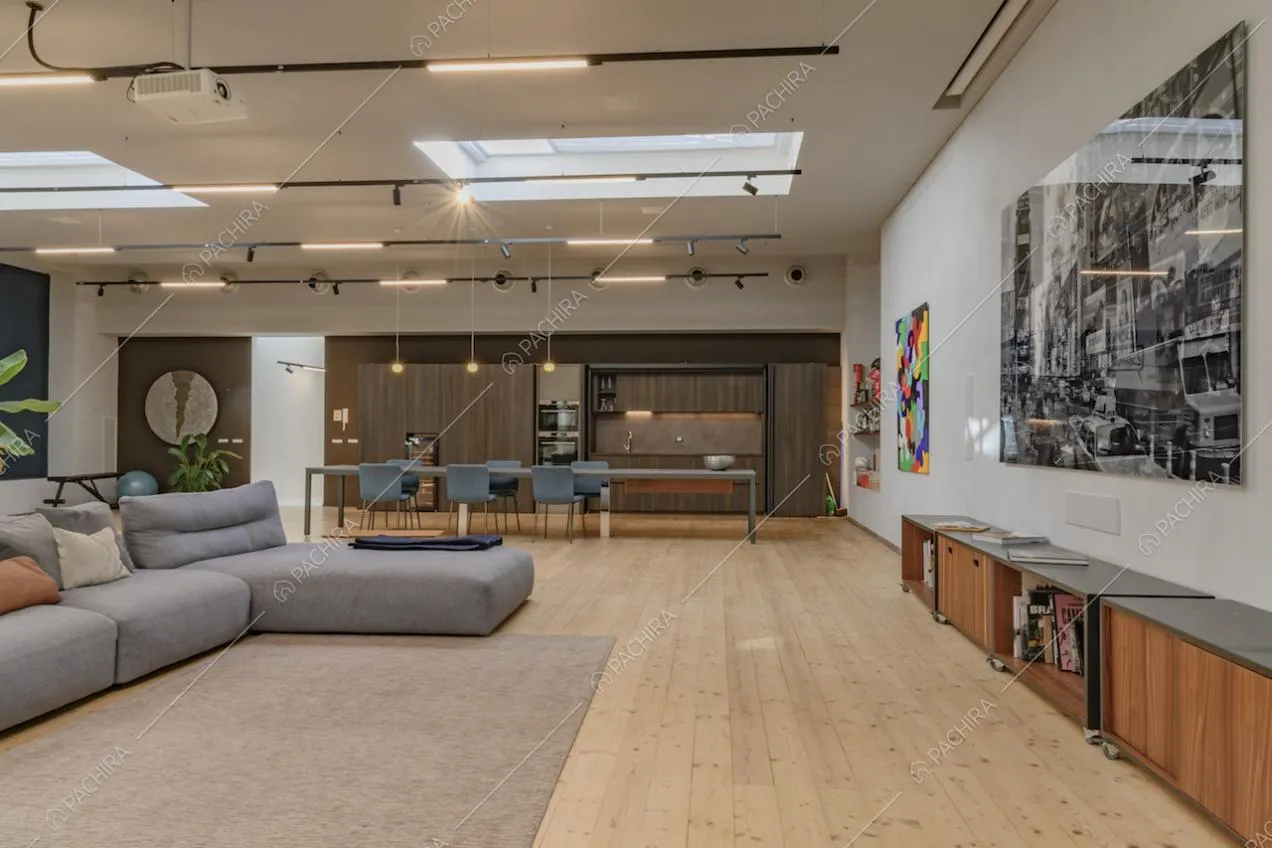 Sala con divano angolare grigio e pavimento in parquet illuminata da lucernari