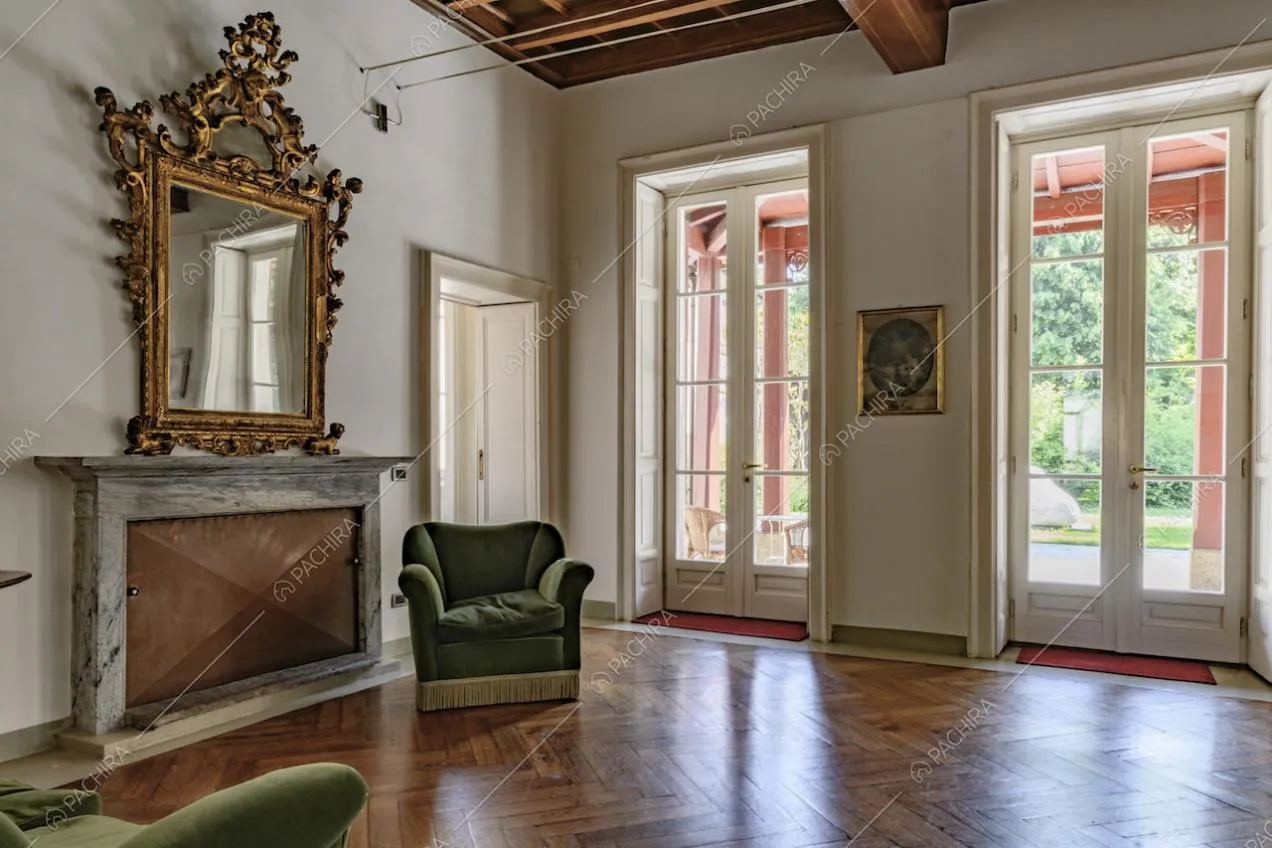 Dalla sala con pavimento in parquet a spina di pesce, pareti bianche e camino chiuso, accesso alla veranda tramite porte-finestre