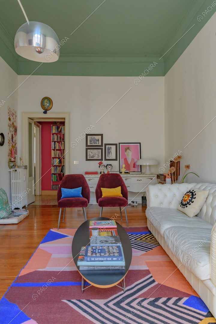 Salotto dal soffitto verde con boiserie, pareti bianche, divano in pelle, tavolino e poltrone di design