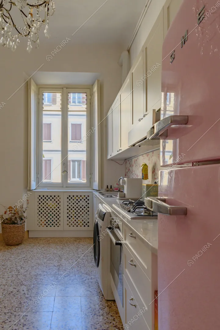 Nella cucina bianca a parete piastrelle a gas, frigorifero rosa confetto di design e pareti bianche
