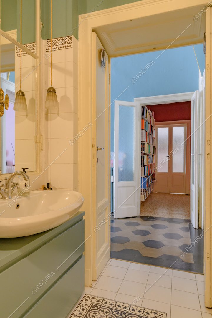 Bagno con piastrelle bianche, mobile verde e vista sull'atrio con pavimento in marmo