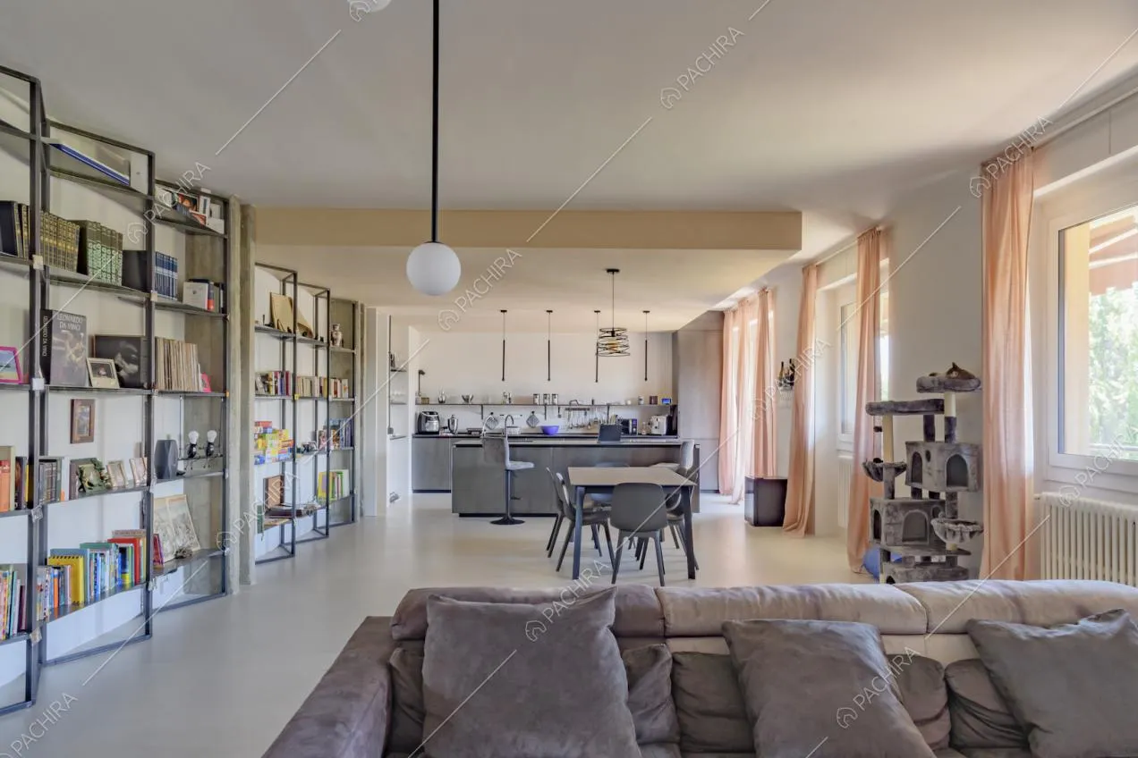 Ampia e luminosa zona living con divano marrone, tavolo e cucina a vista