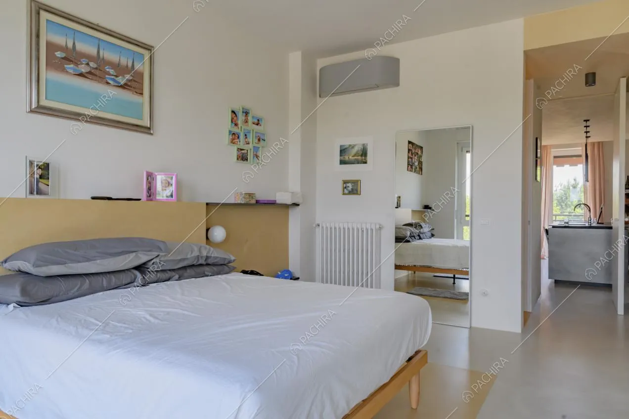 Camera da letto matrimoniale con pavimento in cemento lisciato bianco e vista sull'isola della cucina