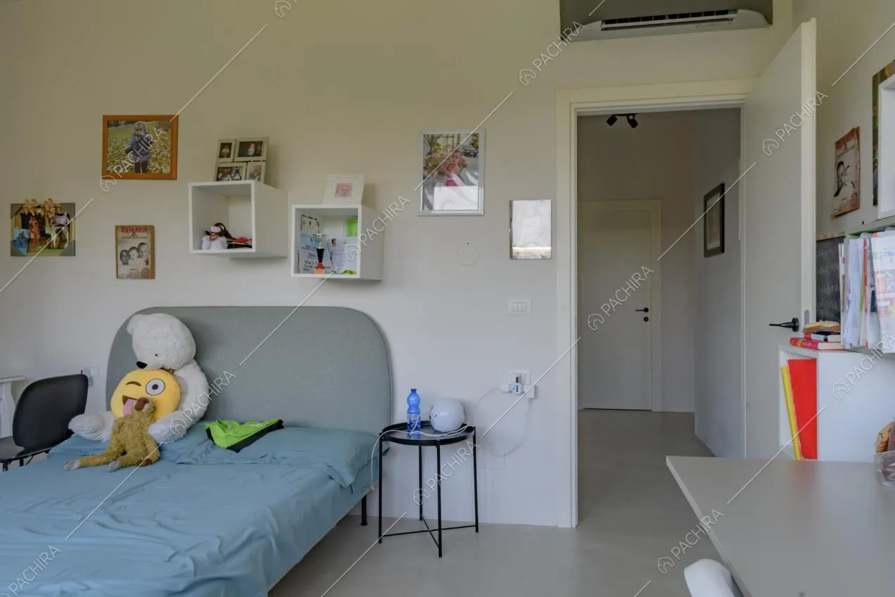 Camera da letto con pavimento in cemento lisciato, scrivania e pareti bianche