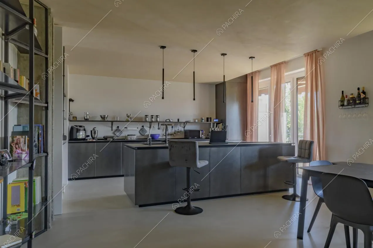 Cucina a vista con isola nell'ampia zona living con pareti bianche e pavimento in cemento lisciato