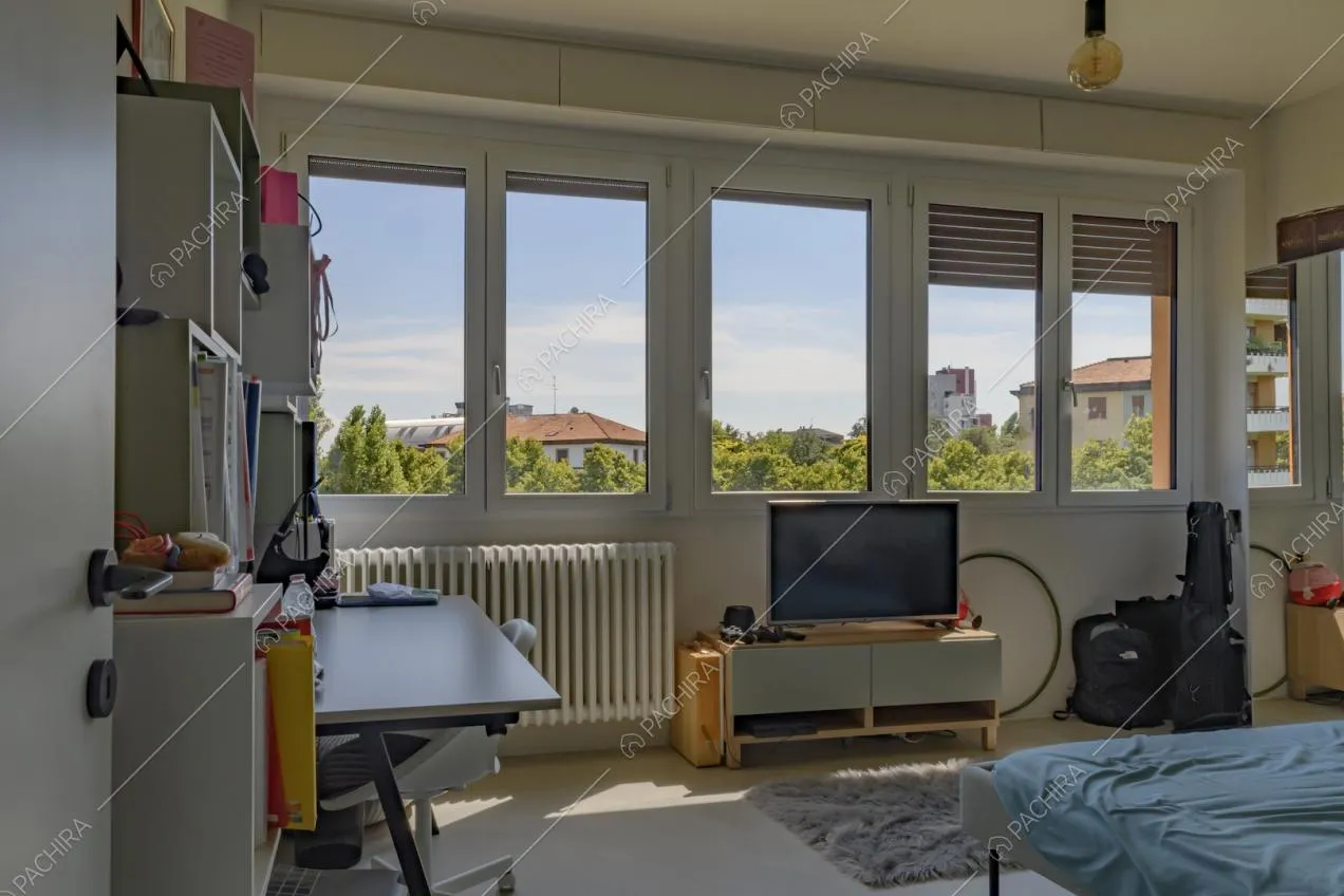 Camera da letto matrimoniale illuminata dalle numerose finestre e con pavimento in cemento lisciato