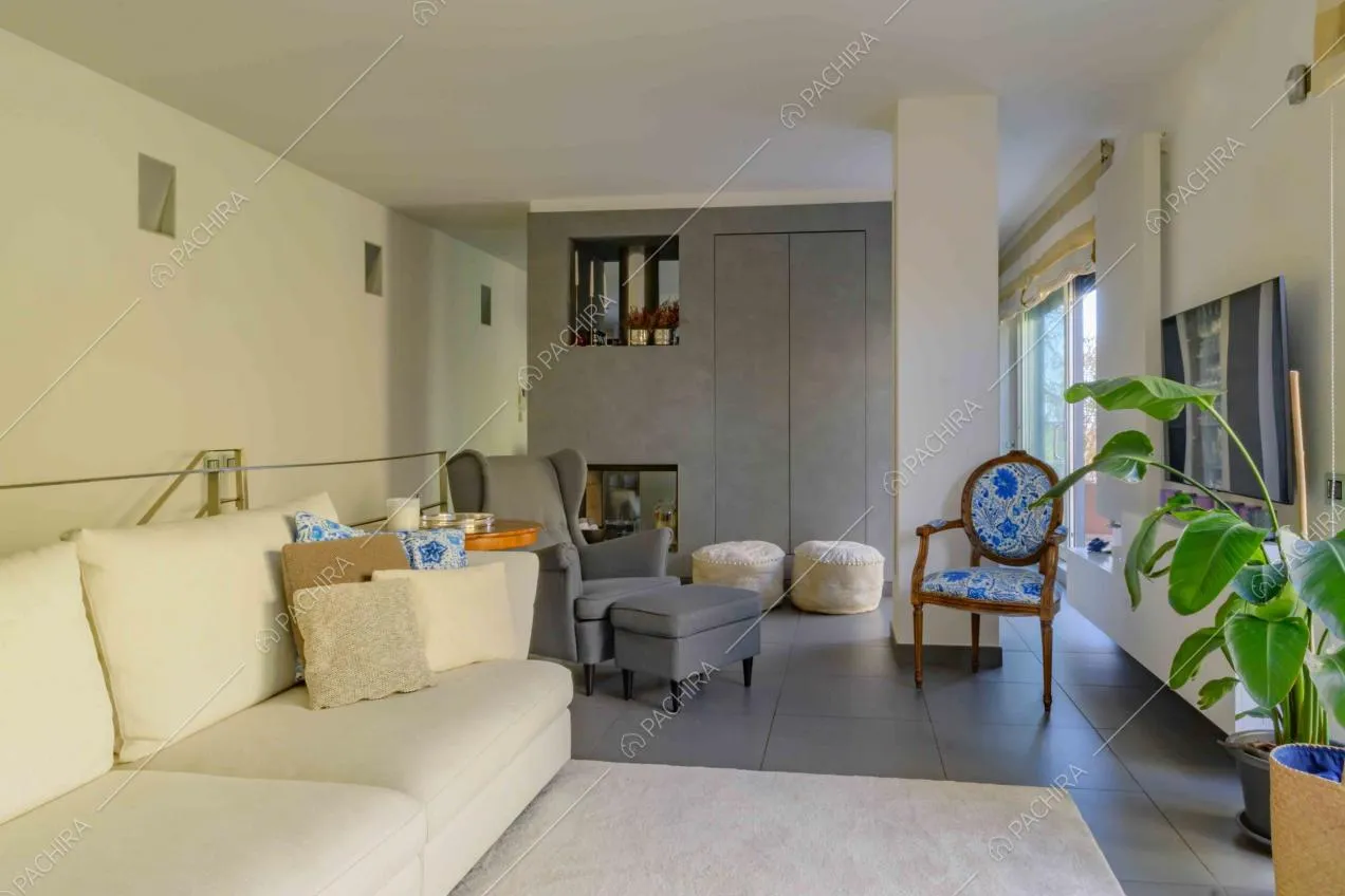 Salotto con divano bianco, poltrona grigia, camino e parete che separa l'ambiente dalla cucina
