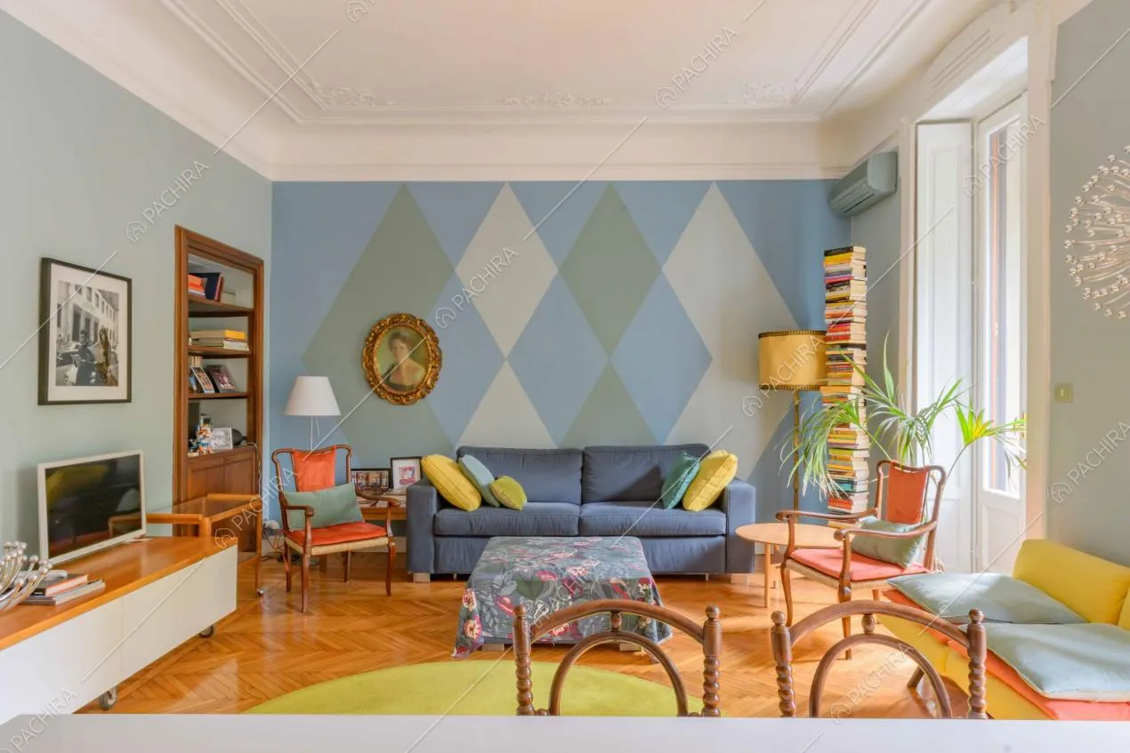 Dal tavolo da pranzo bianco vista sulla sala con boiserie sul soffitto, porte-finestre e pavimento in parquet a spina di pesce