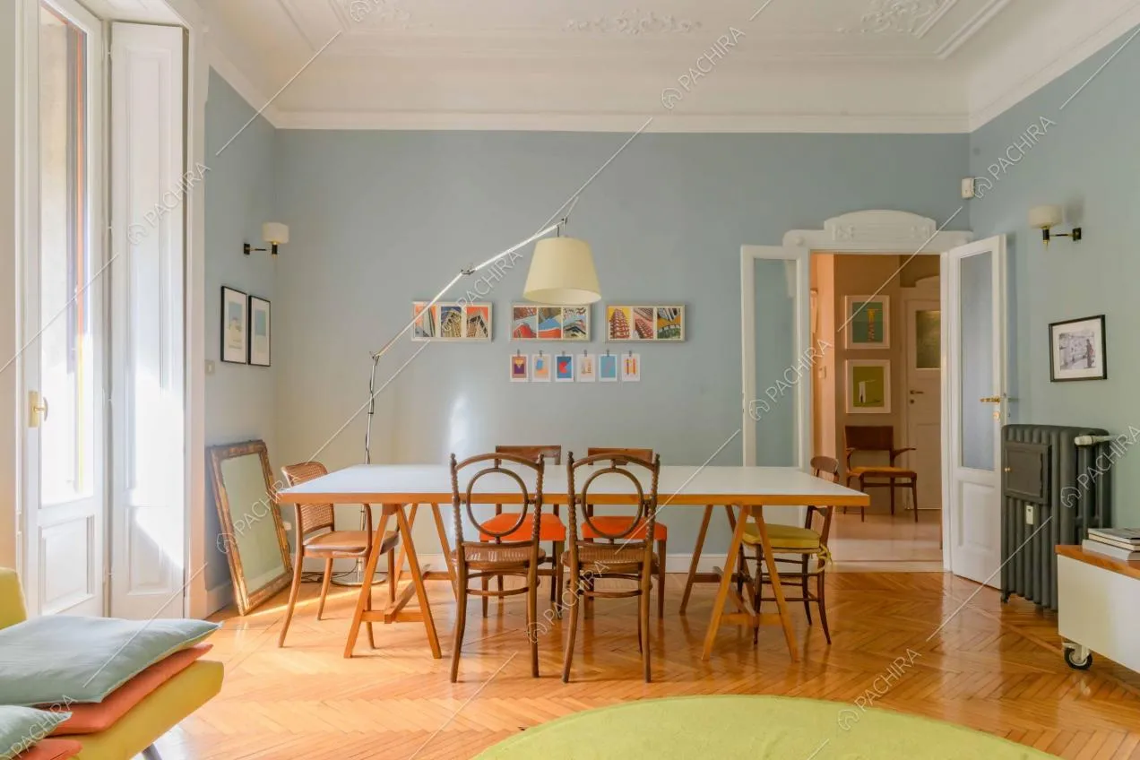 Dal divano del salotto vista sul tavolo da pranzo nella sala dalle pareti azzurre e boiserie sul soffitto