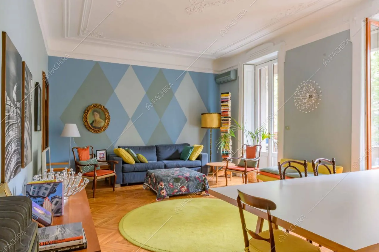 Sala con tavolo da pranzo, divano blu, carta da parati a rombi e boiserie sul soffitto bianco
