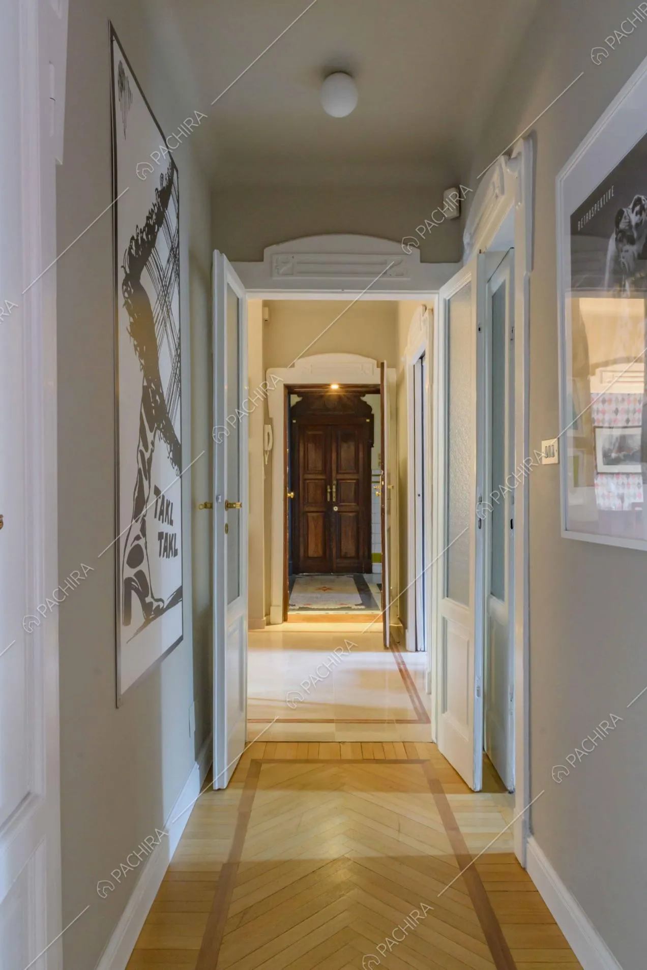 Corridoio dalle pareti beige, con pavimento in parquet a spina di pesce e vista sull'ingresso