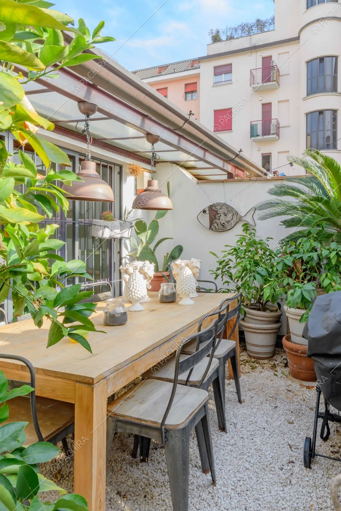 Terrazza con pavimentazione in ciottolato, tavolo da pranzo in legno e sedie in metallo