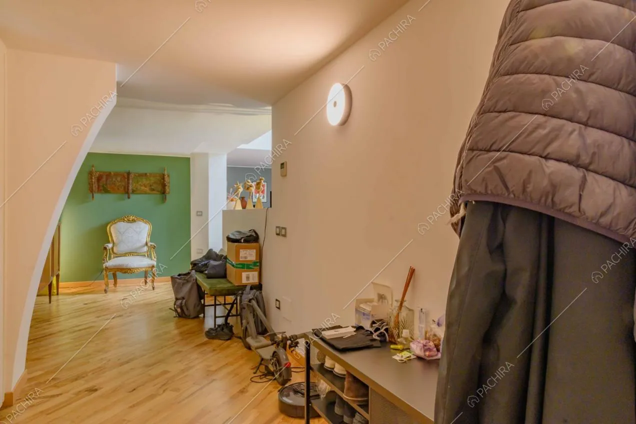 Dalla porta d'ingresso pavimento in parquet, parete verde e scorcio sulla cucina