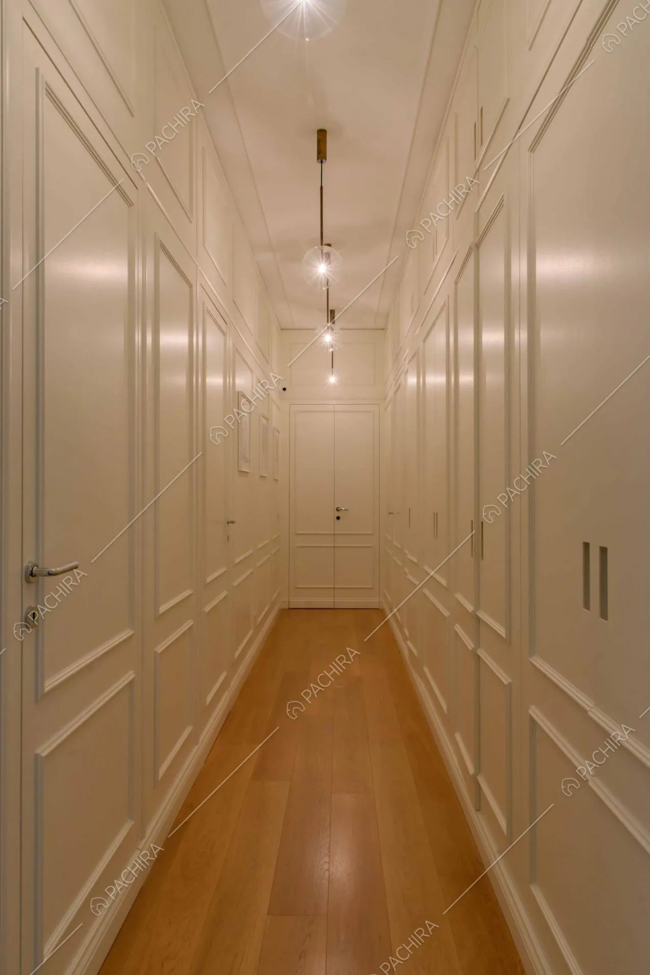Lungo corridoio bianco con boiserie sul soffitto e con pavimento in parquet