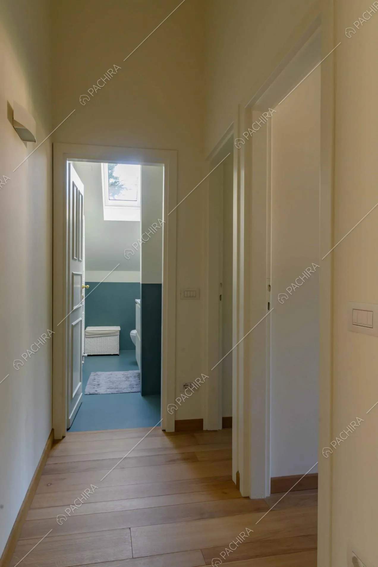 Corridoio con pavimento in parquet e con vista sul bagno dalle pareti bianche e blu petrolio