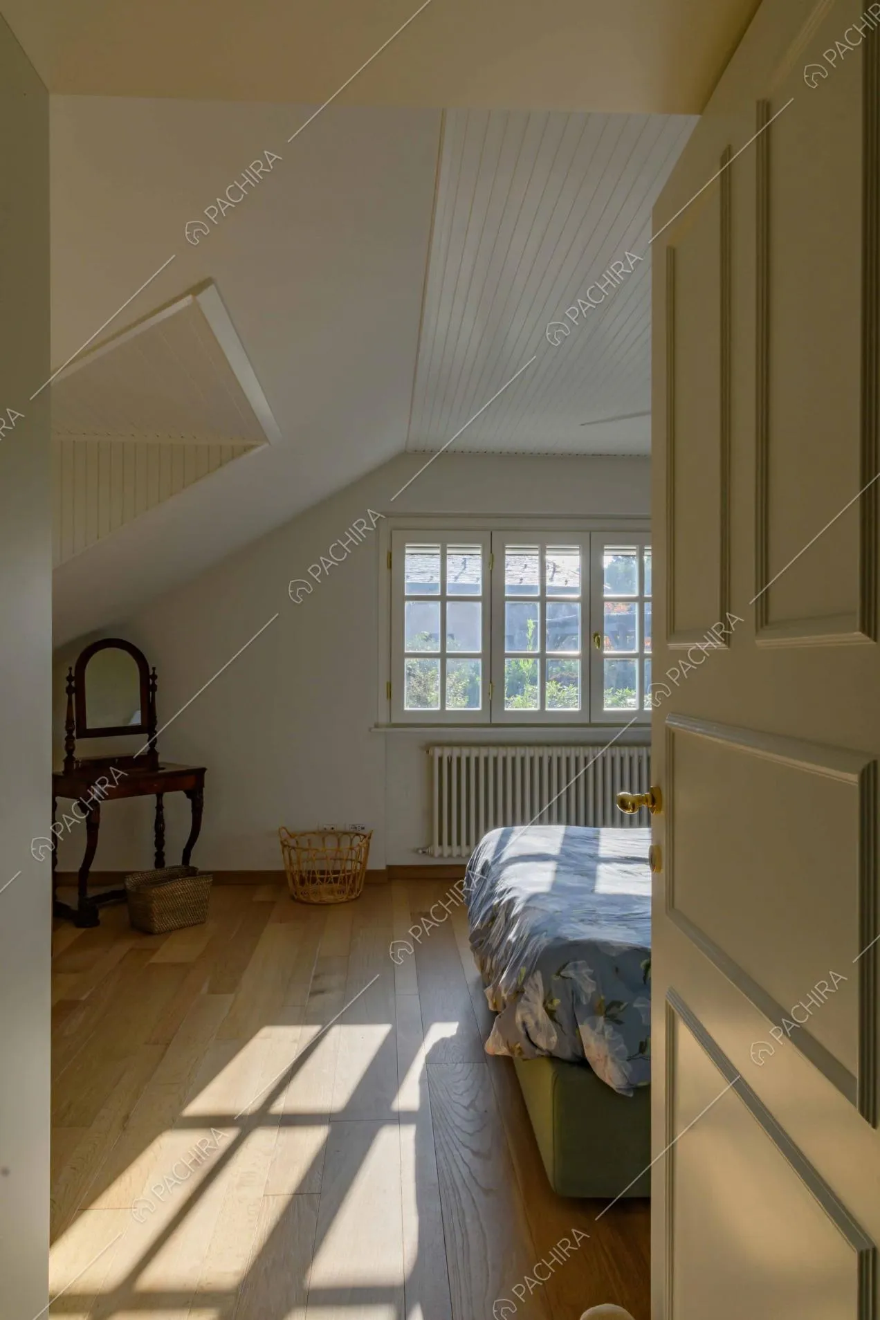 Letto matrimoniale nella luminosa camera con pavimento in parquet e pareti bianche