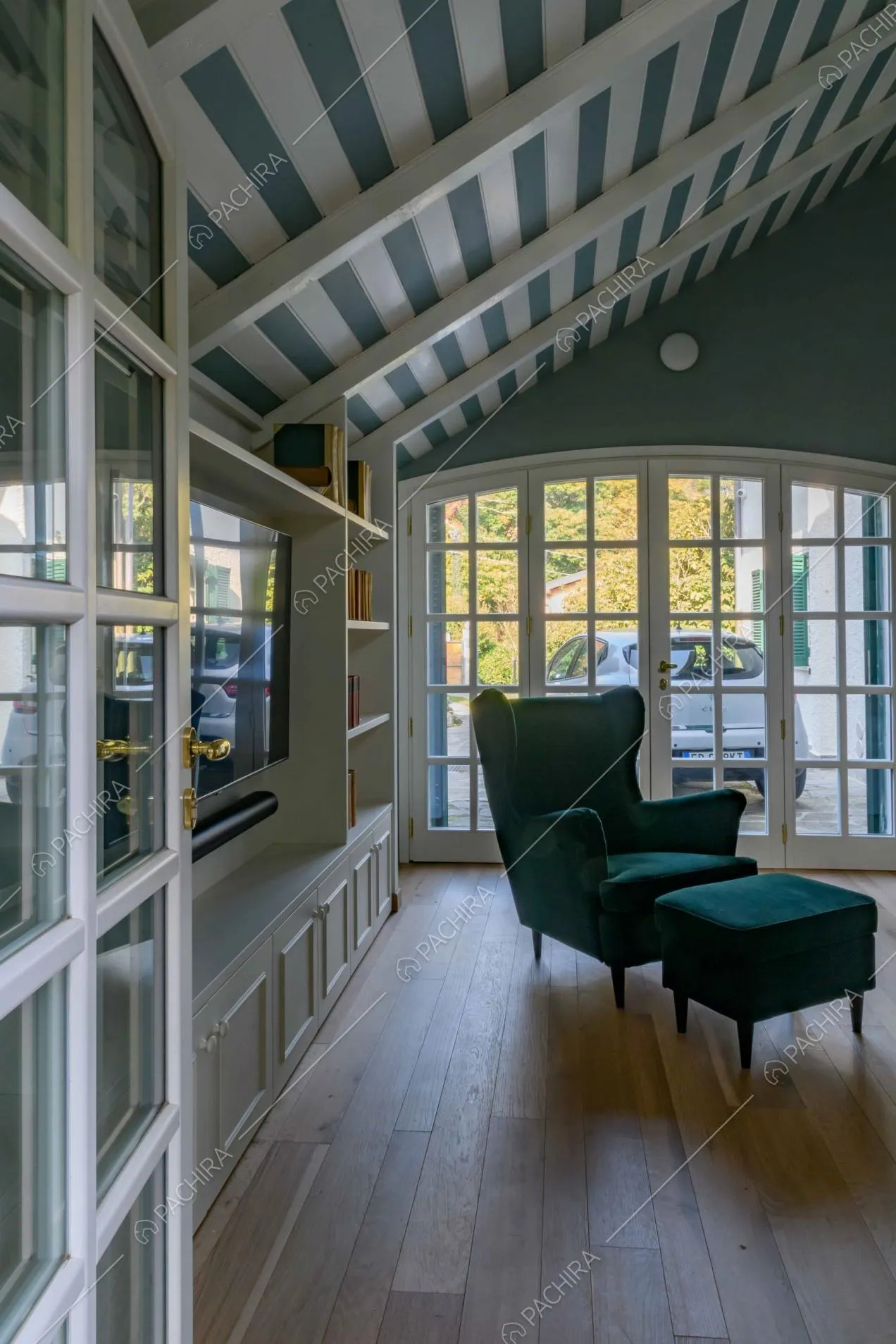 Vista sul salotto con poltrona blu in velluto, pavimento in parquet a listoni e cassetti con boiserie