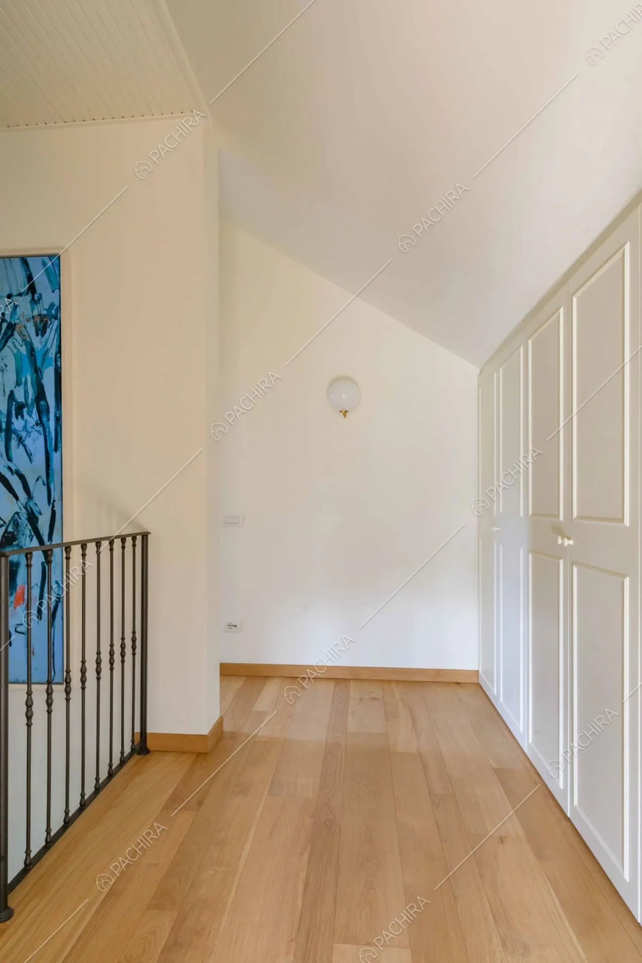 Pareti bianche, pavimento in parquet a listoni e armadi bianchi con boiserie al piano superiore