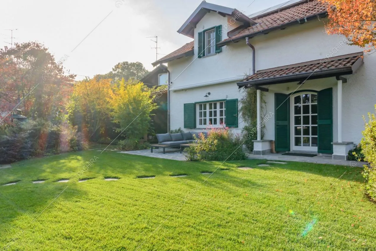 Vista sulla villa bianca a due piani con persiane verdi e sugli alberi del giardino