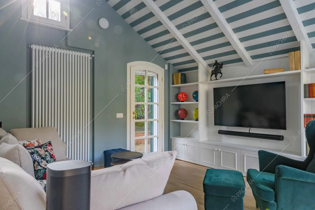 Salotto con soffitto in travi in legno a vista e righe bianche e blu, poltrona in velluto e pavimento in parquet