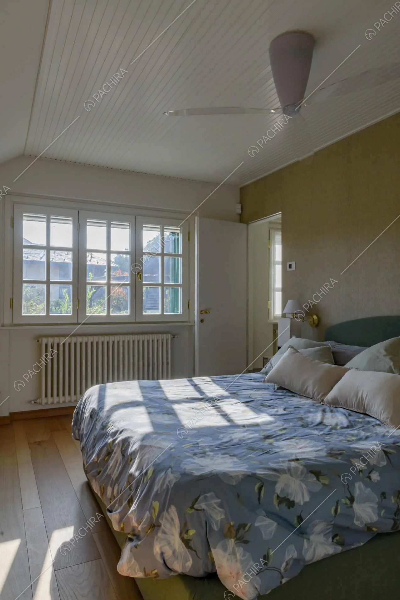 Letto matrimoniale nella camera da letto con grandi vetrate e pavimento in parquet