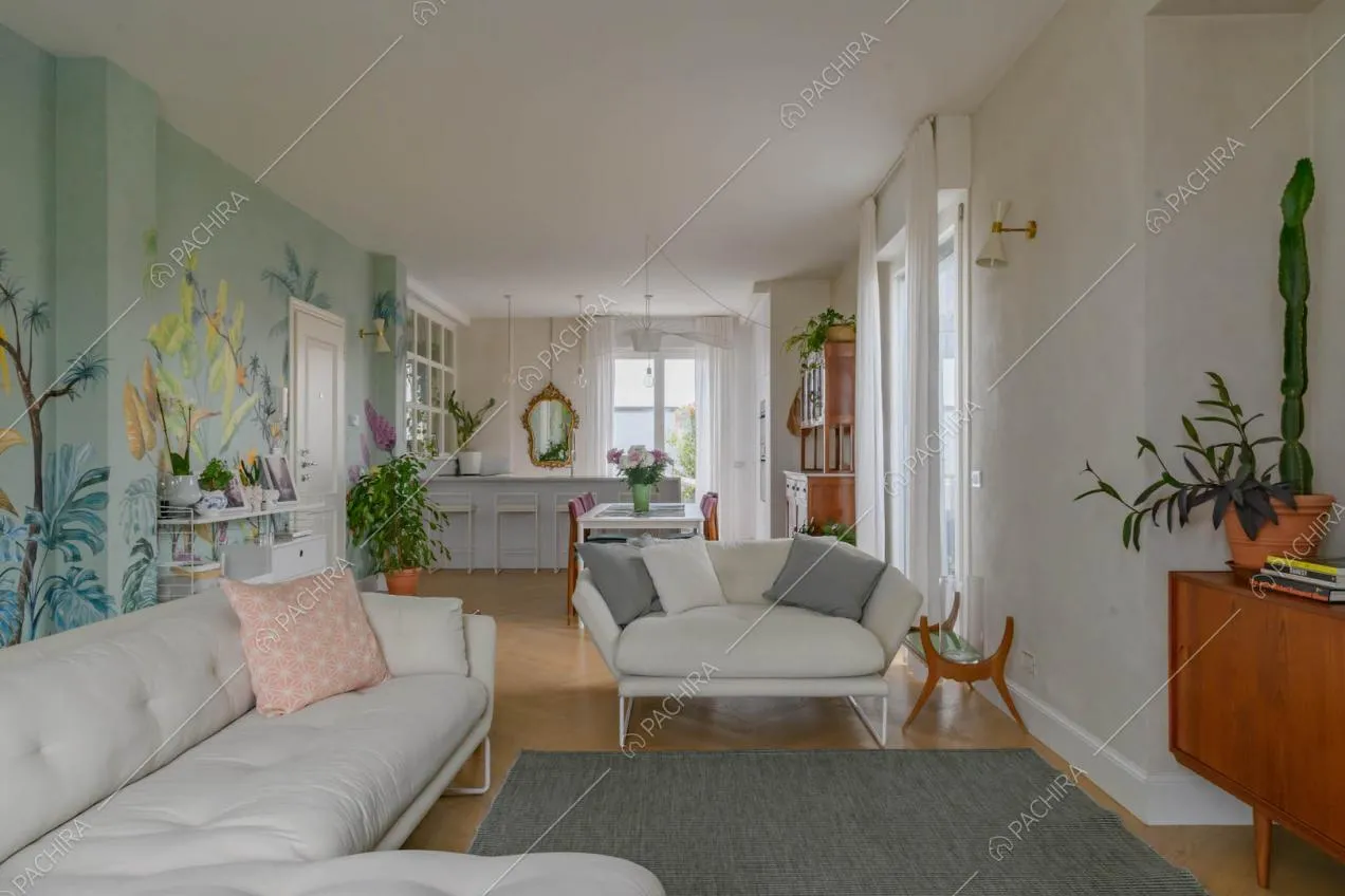 Sala con divani bianchi, pavimento in parquet e carta da parati a fantasia tropicale
