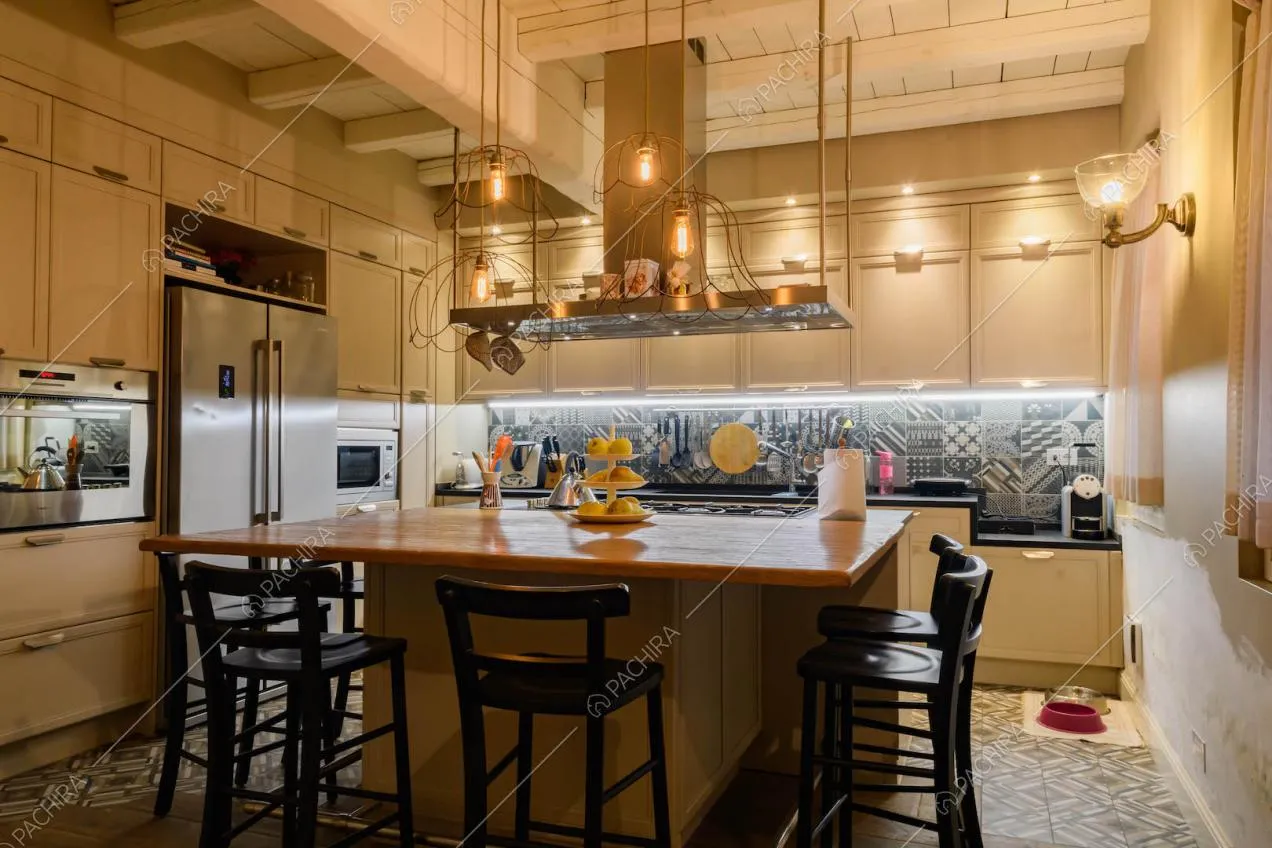 Cucina a isola con bancone in legno, sgabelli neri, cementine e soffitto con travi in legno bianco a vista