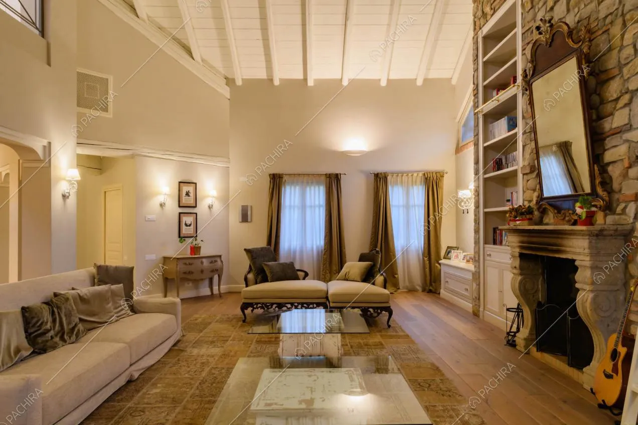 Salotto con alto soffitto bianco in travi in legno, parete in pietra a vista e camino