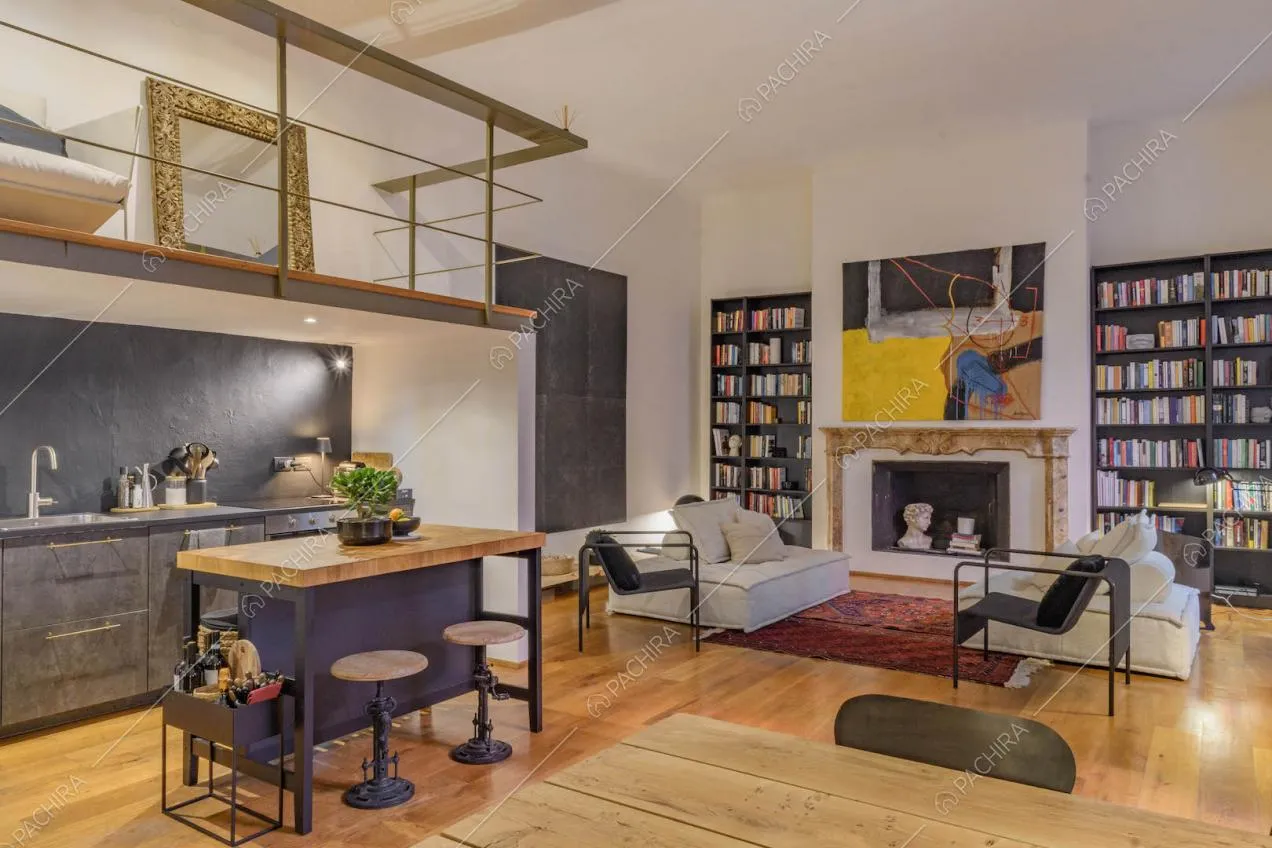 Cucina a vista a isola nella sala con soppalco, divani bianchi e sedie nere di design