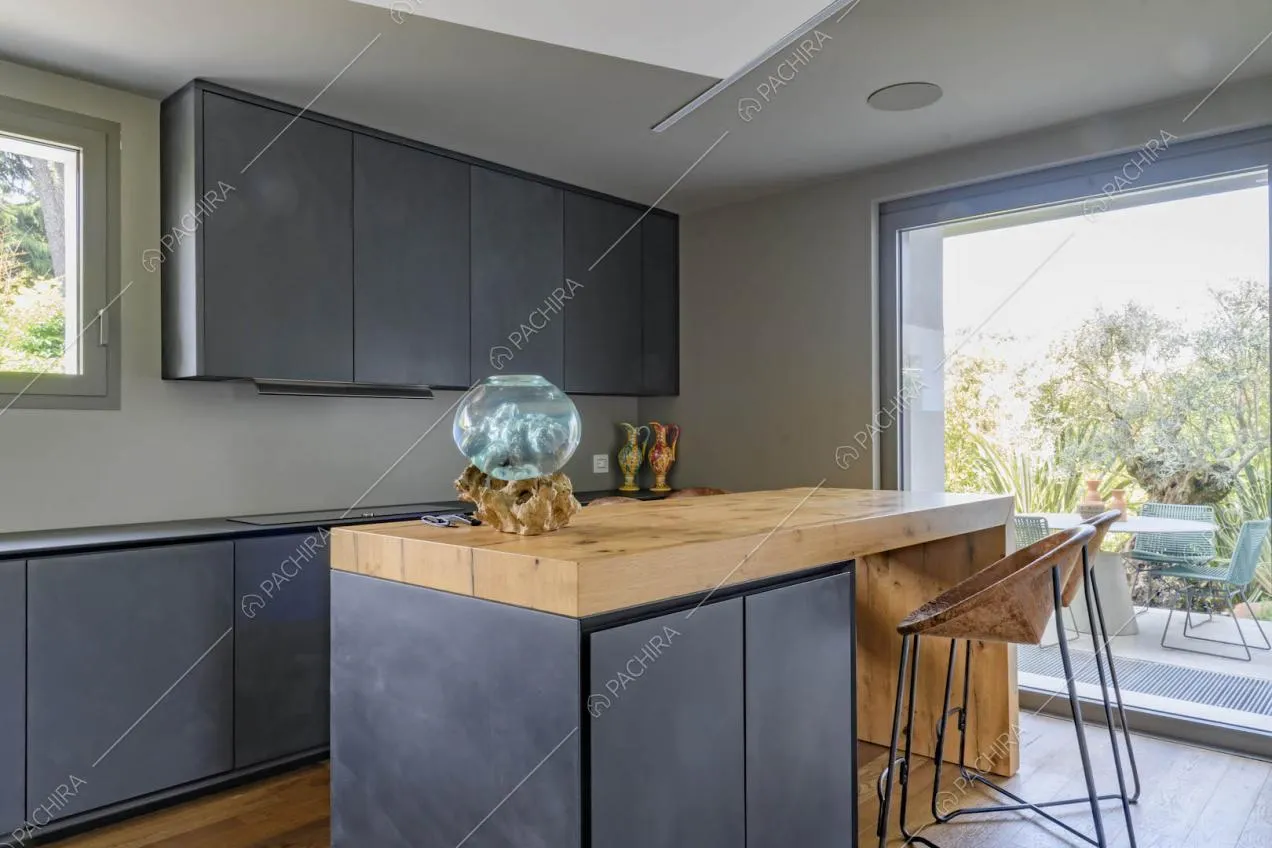 Cucina a isola con piano da lavoro in legno, sgabello, fornelli a induzione e porta-finestra